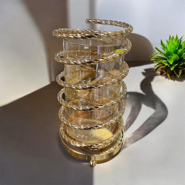 Castiçal em vidro com estrutura em espiral de metal dourado.